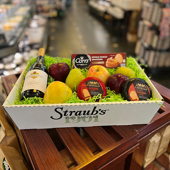 Gift basket with fruits, cheeses, and a bottle of wine on a wooden crate in a grocery store.
