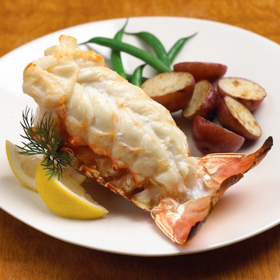 Lobster tail on a plate with lemon wedges, green beans, and potatoes.