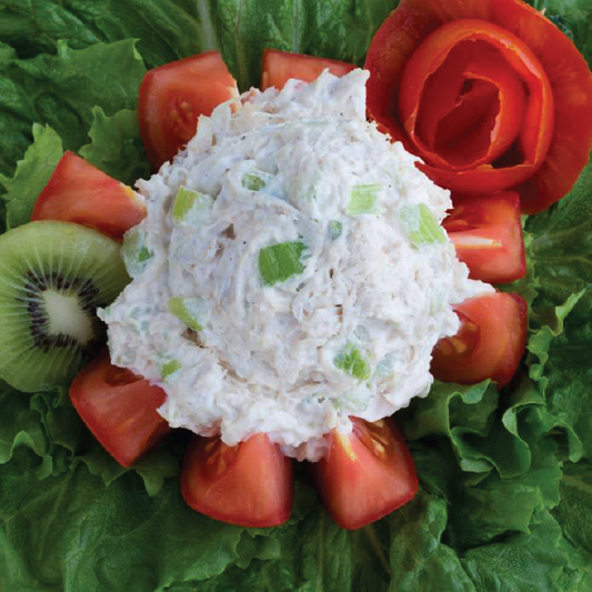 Chicken salad ball surrounded by sliced tomatoes, kiwi, and lettuce on a bed of lettuce