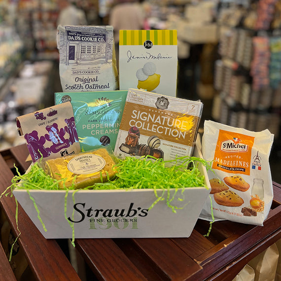 Assorted snacks and treats in a box with 'Straub's Fine Grocers' branding on a store shelf.
