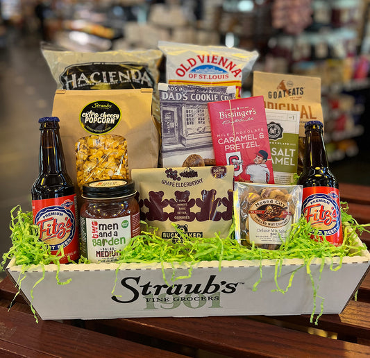 Gift basket with snacks, drinks, and cookies on a wooden table.