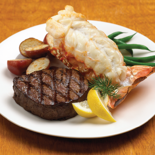 Steak and lobster tail on a plate with lemon and green beans