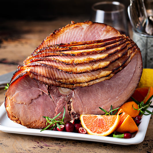 Roasted ham on a platter with orange slices and herbs on a wooden table.