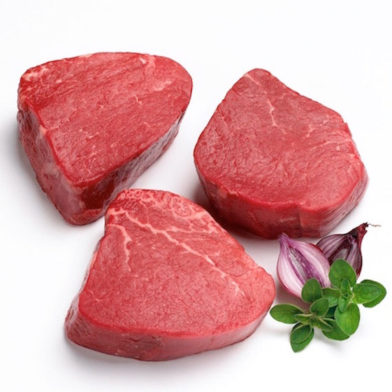 Three pieces of raw red meat with a sprig of thyme and a shallot on a white background