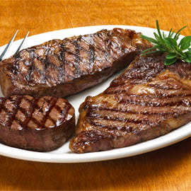 Grilled steaks on a white plate with a wooden background