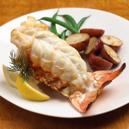Lobster tail on a plate with lemon wedges, green beans, and potatoes.