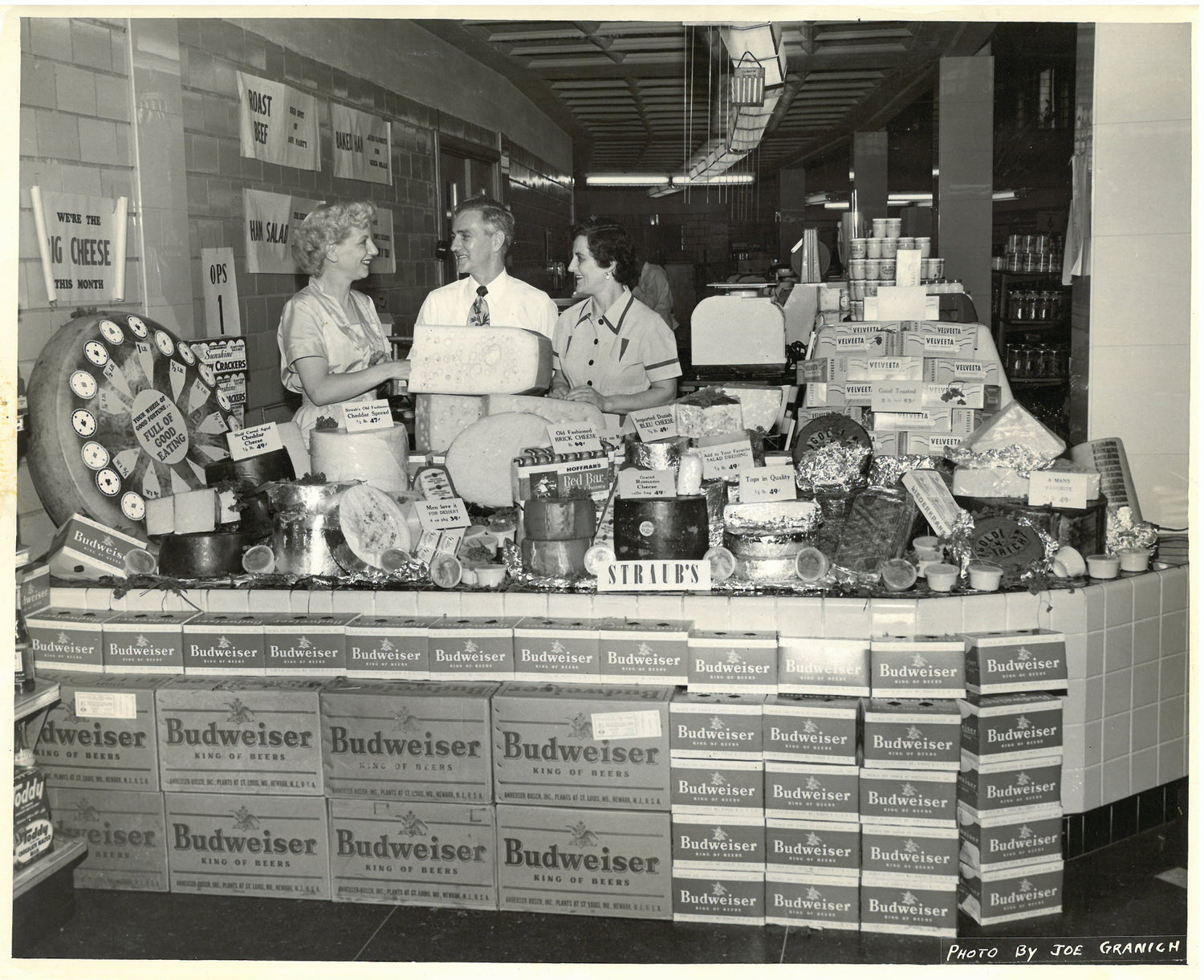Vintage black and white photo of a Budweiser display with people around it.