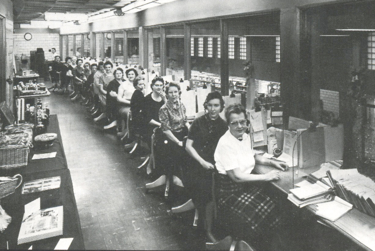 Vintage black and white photo of a large office with rows of desks and people working.