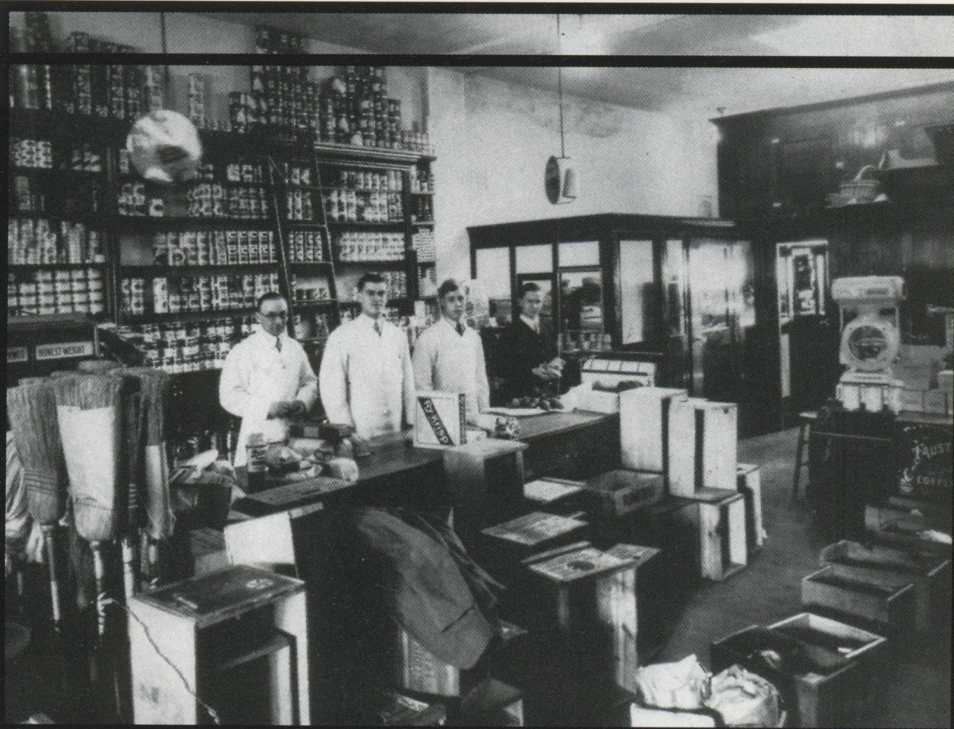Vintage black and white photo of a pharmacy with staff and shelves.