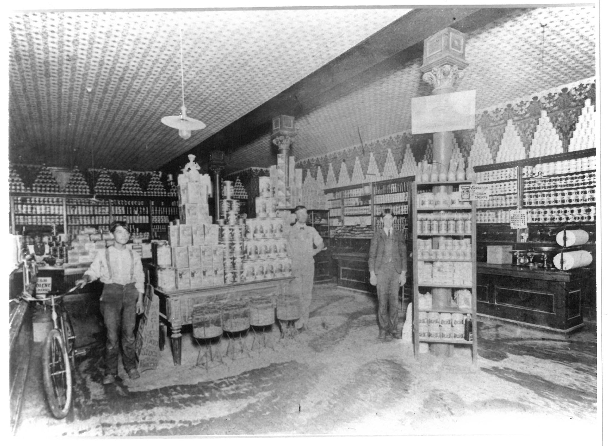 Vintage black and white photo of a pharmacy interior with shelves and people.